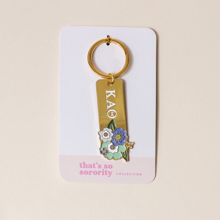 The Darling Effect’s Kappa Alpha Theta Enamel Keychain features “KAΘ” in white, blue, and yellow floral charms—attached to a “that’s so sorority collection” card. The perfect gift for any member!.
