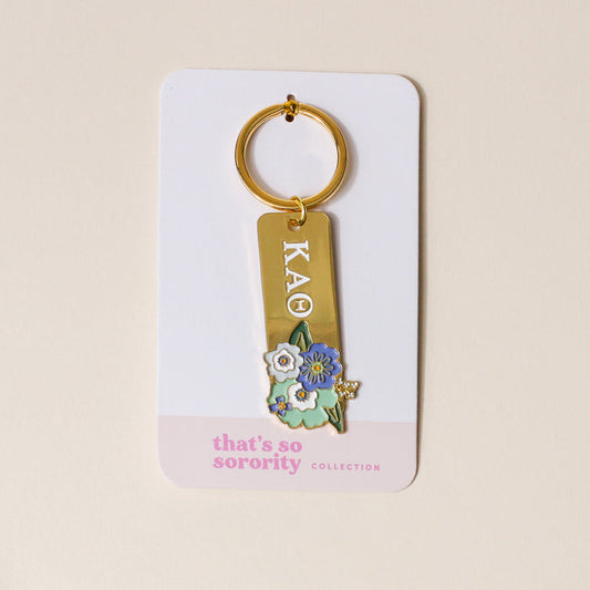 The Darling Effect’s Kappa Alpha Theta Enamel Keychain features “KAΘ” in white, blue, and yellow floral charms—attached to a “that’s so sorority collection” card. The perfect gift for any member!.