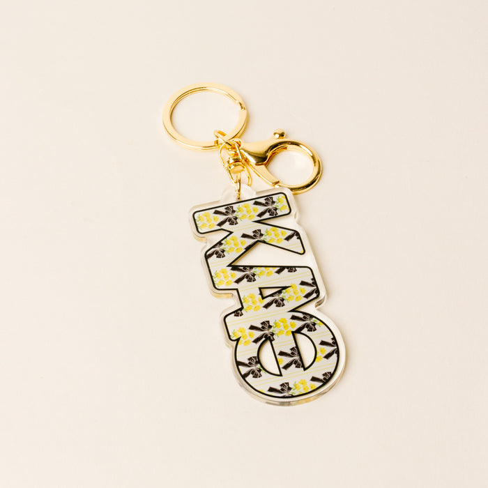 The Darling Effect's Kappa Alpha Theta Oh So Fancy Letter Acrylic Keychain features a large XO charm with a yellow and black floral pattern—an ideal sisterhood gift for any Theta.
