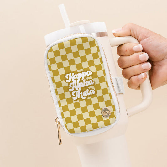 A hand holds a white tumbler with The Darling Effect’s Kappa Alpha Theta Tumbler Fanny Pack—a beige checkered pouch with bold white lettering—ideal for sorority recruitment, against a soft beige background.