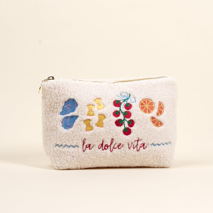 The Darling Effect La Dolce Vita Teddy Pouch is a cream sherpa zip pouch with embroidered mushrooms, pasta, tomatoes, and orange slices above “la dolce vita” in red script.