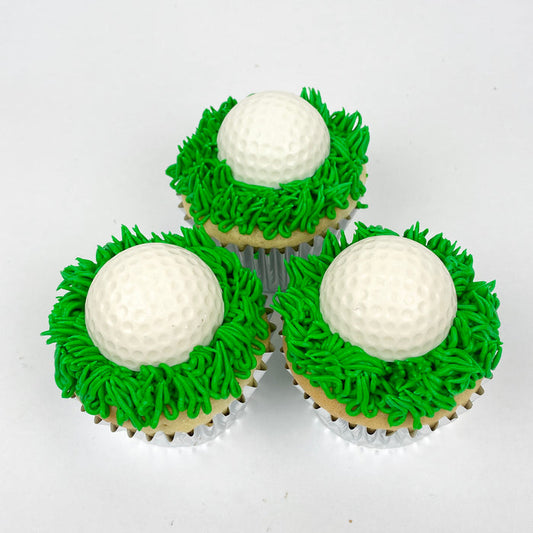 Three cupcakes iced in grass green buttercream and topped with a white chocolate golf ball.