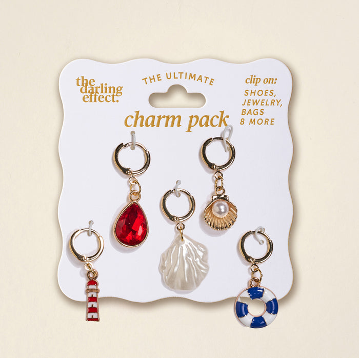 Lighthouse Glow The Ultimate Charm Pack by The Darling Effect includes five gold clip-on charms—a red gemstone, shell, pearl in a scallop shell, red-and-white striped lighthouse, and blue-and-white lifebuoy—perfect for Make a Statement Necklaces or Scrunchie Charm Sets.