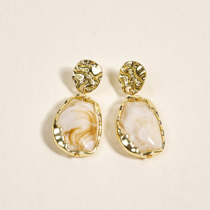 The Darling Effect's Liquid Gold Standout Earrings feature round textured gold studs and irregular white marbled stones with a high-shine finish, displayed on a light cream background.