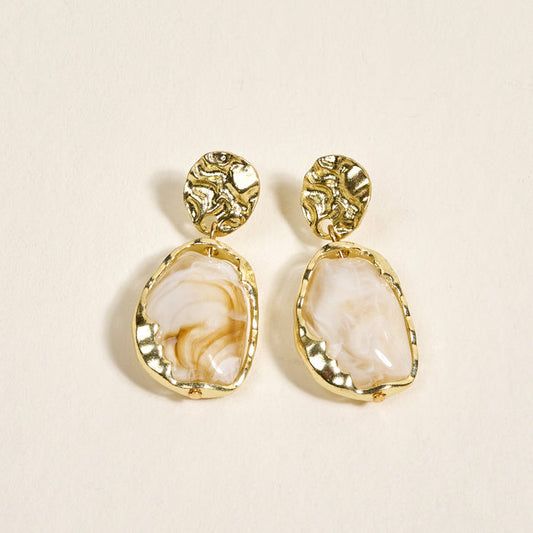 The Darling Effect's Liquid Gold Standout Earrings feature round textured gold studs and irregular white marbled stones with a high-shine finish, displayed on a light cream background.