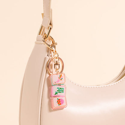 A close-up of The Darling Effect’s Mahjong Tiles Acrylic Keychain, a cream-colored handbag accessory featuring three pastel acrylic keychains with abstract designs—a cute and stylish way to elevate any look.