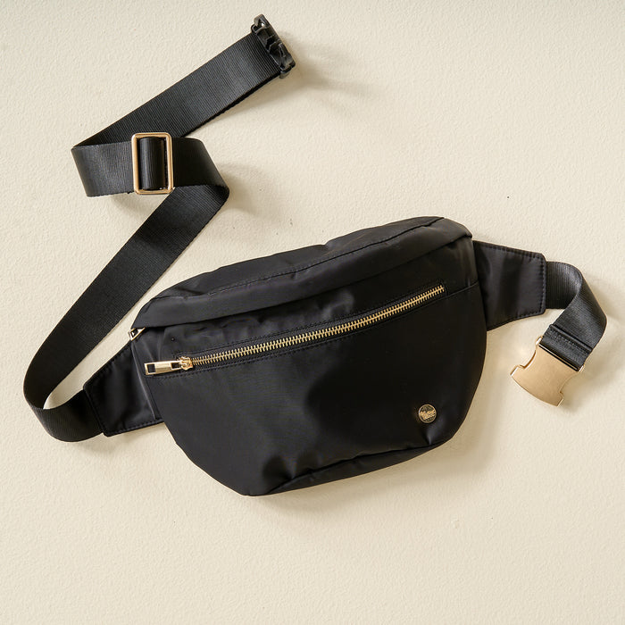 The Darling Effect's Midnight Black XL All You Need Belt Bag features a gold zipper, small round metal logo, and an adjustable black strap with a gold buckle, shown lying flat on a light-colored surface.