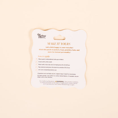 A square instruction card for The Darling Effect's Mother Mix & Match Iron-On Patch displays gold text with use directions and a warning on a white scalloped-edged background, helping you easily personalize items with colorful designs.