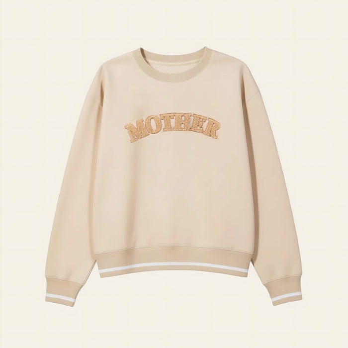The Darling Effect's Mother Signature Crew is a beige sweatshirt with soft fabric, bold textured tan "MOTHER" lettering on the chest, and finished with white stripes on the cuffs and hem.