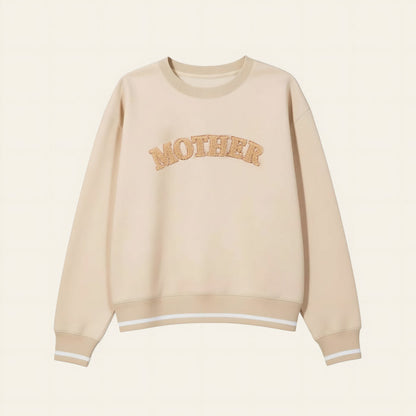The Darling Effect's Mother Signature Crew is a beige sweatshirt with soft fabric, bold textured tan "MOTHER" lettering on the chest, and finished with white stripes on the cuffs and hem.