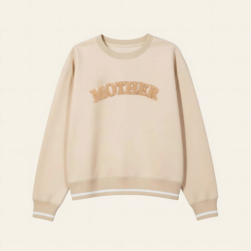 The Darling Effect's Mother Signature Crew is a beige sweatshirt with soft fabric, bold textured tan "MOTHER" lettering on the chest, and finished with white stripes on the cuffs and hem.