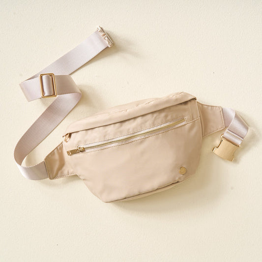 The Darling Effect’s Natural Beige XL All You Need Belt Bag features a gold zipper, matching clasp, adjustable strap with plastic buckle and metal slider, shown lying flat on a light surface.