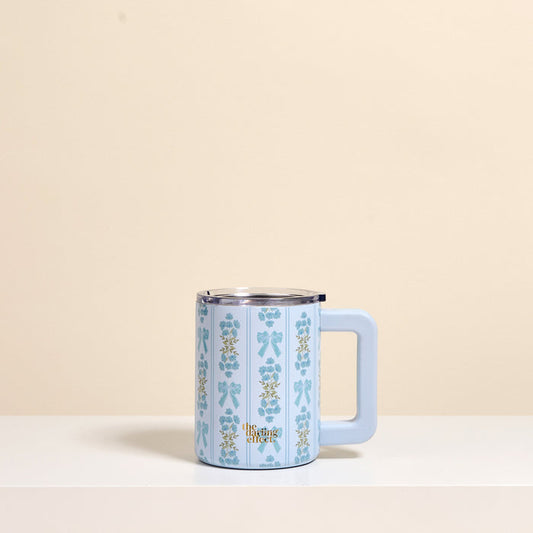 The Oh So Fancy Blue 14 oz Insulated Mug by The Darling Effect features a vertical floral pattern, large handle, and double-wall insulation to keep drinks hot or cold. "The Met" appears near the base. Shown on a plain beige background.