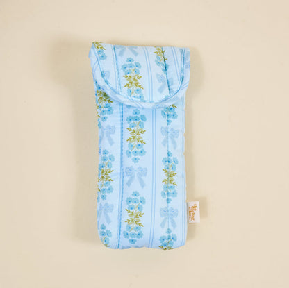 The Darling Effect’s Oh So Fancy Blue Puffy Sunglasses Case features padded blue material with light blue stripes, floral design with bows, and a secure magnetic flap for stylish protection.