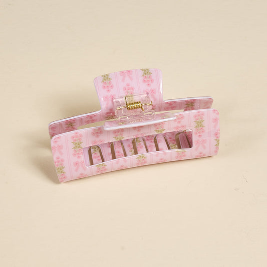 The Darling Effect’s Oh So Fancy Pink Claw Clip features a floral print and rectangular cutout for a stylish, secure hold, shown on a plain beige surface.