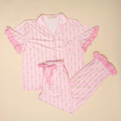 The Darling Effect's Oh So Fancy Pink Slumber Party Pajama Pants Set features a relaxed fit with a short-sleeved, button-up top and long pants in ultra-soft floral print fabric with ruffled trim, shown laid flat on a beige background.