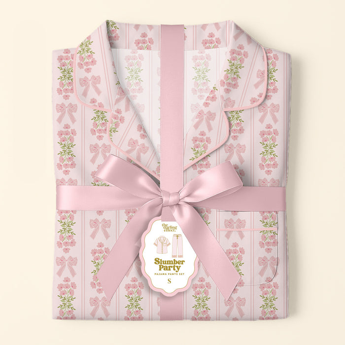 The Darling Effect's Oh So Fancy Pink Slumber Party Pajama Pants Set, featuring pink floral and bow patterns in ultra-soft fabric, arrives wrapped with a wide satin ribbon and decorative tag—an ideal cozy gift set.