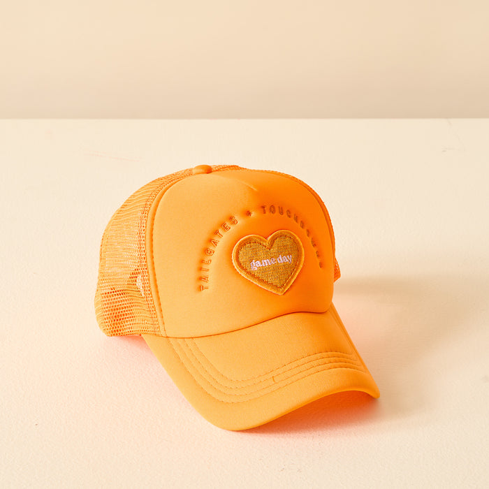 The Darling Effect Orange Game Day Trucker Hat features a heart-shaped foam+day patch and raised embroidered text on the front, perfect for showing team spirit. Displayed against a light beige background.
