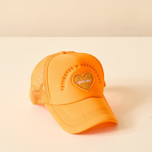 The Darling Effect Orange Game Day Trucker Hat features a heart-shaped foam+day patch and raised embroidered text on the front, perfect for showing team spirit. Displayed against a light beige background.