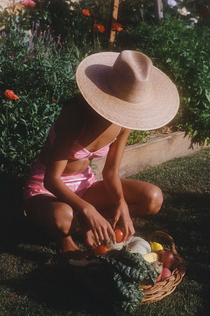 A person wearing a Palma Wide Fedora hat while gathering vegetables in a garden.