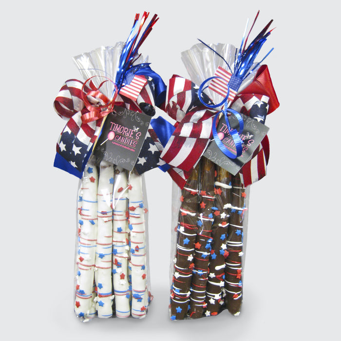 One bag of six white chocolate-covered pretzel rods and one bag of six dark chocolate-covered pretzel rods. Each rod is decorated with red, white, and blue drizzle and topped with star-shaped sprinkles. Each bag is tied with a festive patriotic ribbon and a mini USA flag.