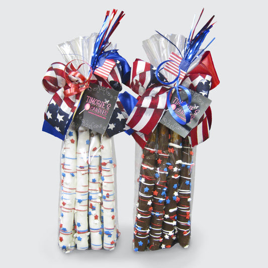 One bag of six white chocolate-covered pretzel rods and one bag of six dark chocolate-covered pretzel rods. Each rod is decorated with red, white, and blue drizzle and topped with star-shaped sprinkles. Each bag is tied with a festive patriotic ribbon and a mini USA flag.