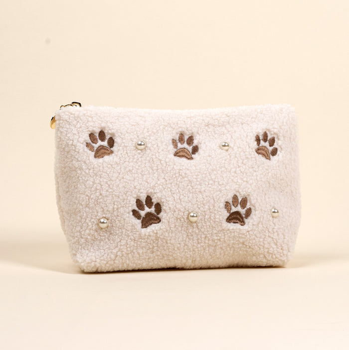 The Darling Effect’s Paws & Pearls Teddy Pouch is a fluffy white sherpa accessory featuring embroidered brown paw prints and pearl accents.