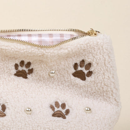 The Darling Effect’s Paws & Pearls Teddy Pouch features a cream sherpa finish with brown paw prints, round pearl-like accents, a gold zipper, and pink and white striped lining—an adorable addition to your teddy pouch collection.