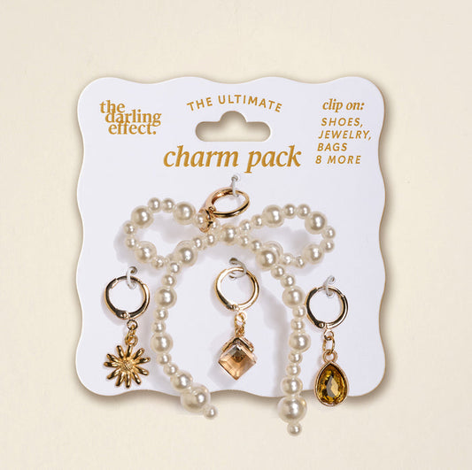 The Darling Effect’s Pearl Party The Ultimate Charm Pack includes four gold and pearl charms—a pearl bracelet, sunburst, square gem, and teardrop gem—on a display card. Perfect for shoes, jewelry, bags, or pairing with statement necklaces.