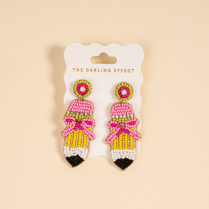 The Darling Effect's Pencil Me In Beaded Earrings feature hand-beaded, pencil-shaped designs in pink, yellow, and black with a cute pink bow and green accents—perfect for adding a pop of color to any outfit.