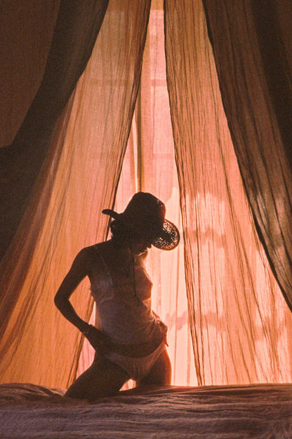 Silhouette of a person wearing a brown straw cowboy hat, with soft light filtering through curtains