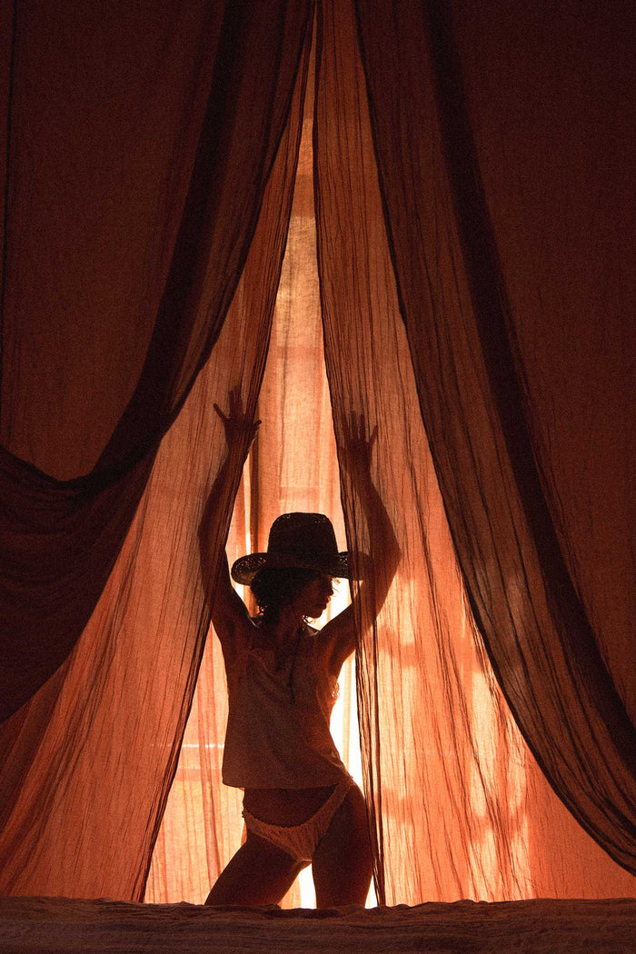 Silhouette of a person wearing a straw cowboy hat behind sheer curtains
