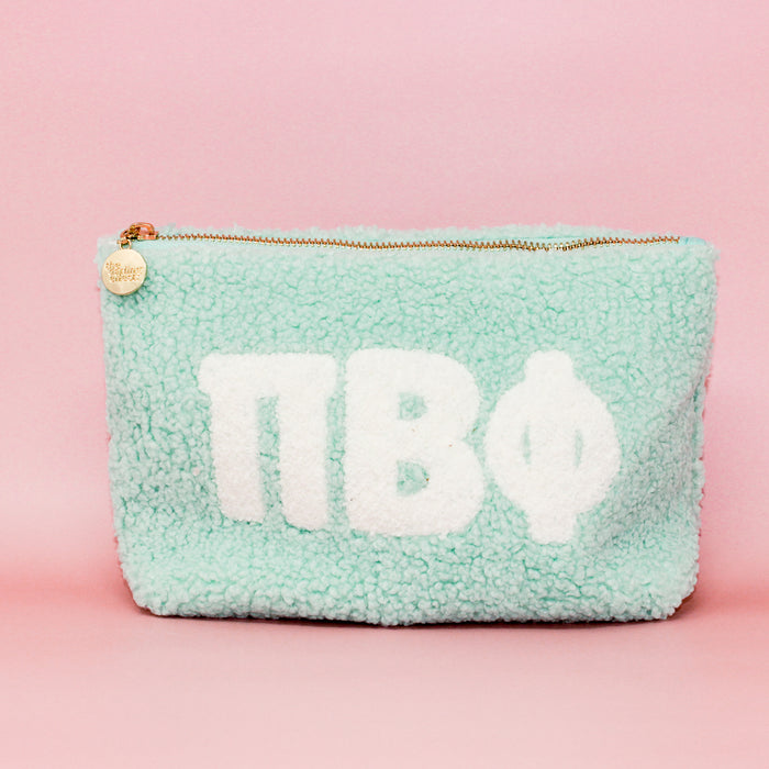 The Darling Effect’s Pi Beta Phi Aqua Teddy Letter Pouch features soft aqua fuzz, bold white ΠΒΦ letters, and a gold zipper with charm—ideal as a stylish sorority accessory or cute travel pouch.