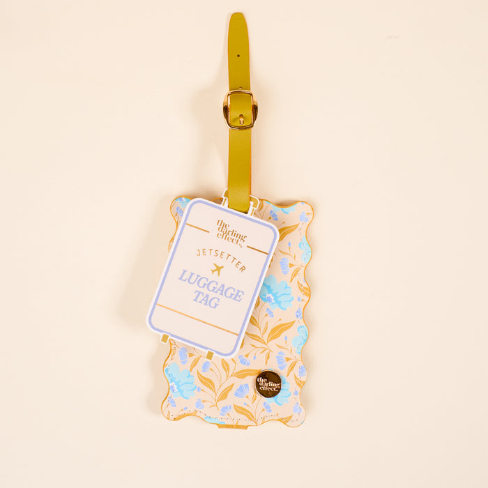 The Darling Effect’s Poppin' Petals Aqua Jetsetter Luggage Tag features a yellow strap, scalloped edges, a yellow and blue floral design, privacy flap, and “JETSETTER LUGGAGE TAG” label on a light beige background.