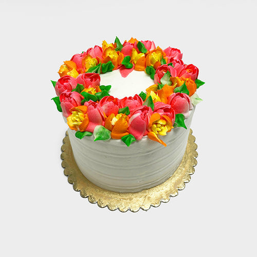 A white Pretty Spring Floral cake decorated with orange, yellow, and pink flowers on top