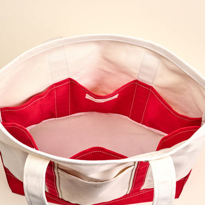 A top view of The Darling Effect’s Red The Signature Canvas Tote Bag shows its red and white fabric, durable handles, multiple inner pockets, neat stitching, and a spacious empty interior—perfect for everyday use.