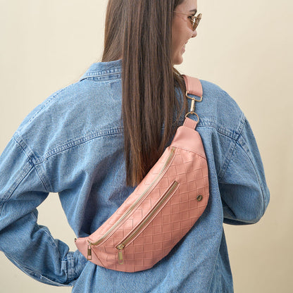 Woman with long brown hair wears sunglasses, a blue denim jacket, and The Darling Effect's Rose Trendy Luxe Belt Bag with gold zippers, posing with her back to the camera against a beige background.