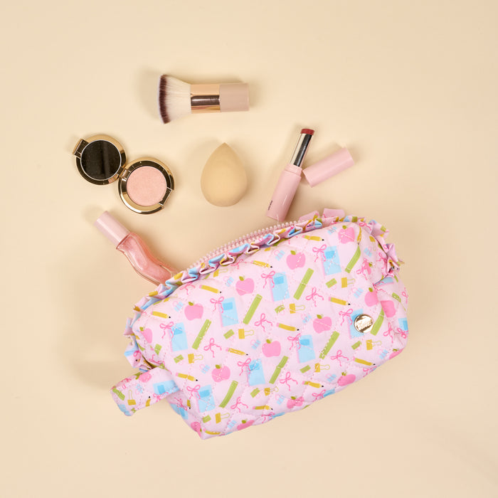 The Darling Effect's School's In Session Essentials Quilted Cosmetic Pouch, featuring gift and lipstick designs, sits open to reveal makeup must-haves—brush, blush compact, sponge, lipstick, and gloss—against a beige background.