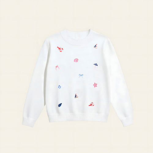 The Darling Effect’s Seaside Haven Refined Knit Sweater is a white crewneck adorned with red embroidered lobsters, blue sailboats and bows, and pink seashells—a charming staple for any wardrobe.
