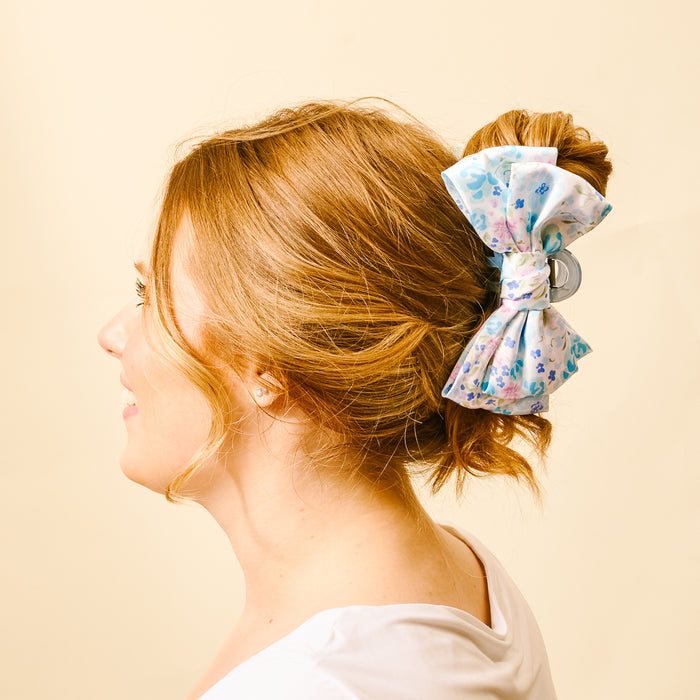 A woman with auburn hair in a messy bun styles it with the-darling-effect’s Secret Garden Blue Satin Bow Claw Clip—an eye-catching accessory perfect for updos.