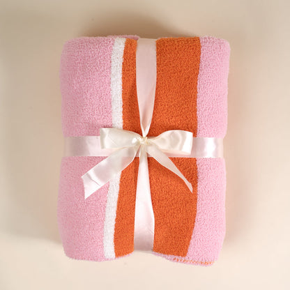 The Sicily Stripes Pink Cozy Dreams Luxe Blanket by The Darling Effect features pink, orange, and white stripes, a plush microfiber texture, and comes folded with a white satin bow, displayed on a light beige background.