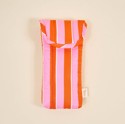 The Darling Effect’s Sicily Stripes Pink Puffy Sunglasses Case features vertical orange and pink stripes, a magnetic flap closure, and a side fabric tag, shown against a plain beige background.