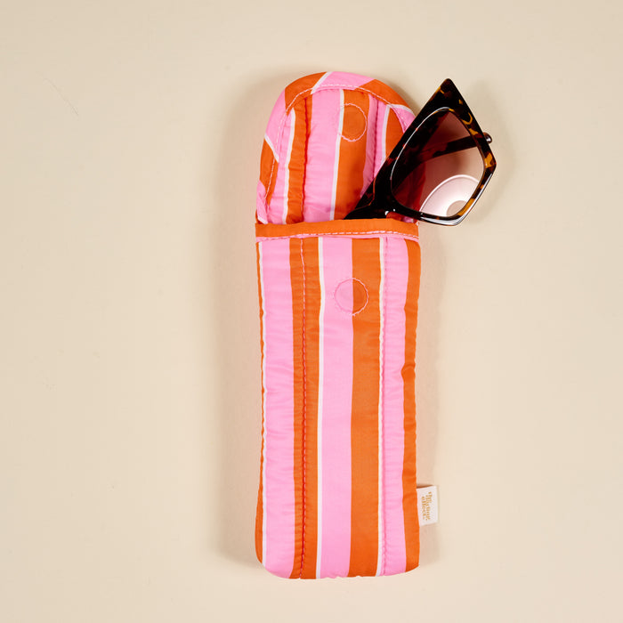 Sunglasses partially tucked into The Darling Effect's Sicily Stripes Pink Puffy Sunglasses Case, featuring a magnetic flap closure, rest on a neutral beige surface.