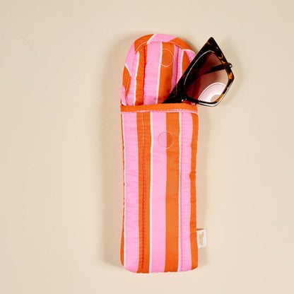Sunglasses partially tucked into The Darling Effect's Sicily Stripes Pink Puffy Sunglasses Case, featuring a magnetic flap closure, rest on a neutral beige surface.