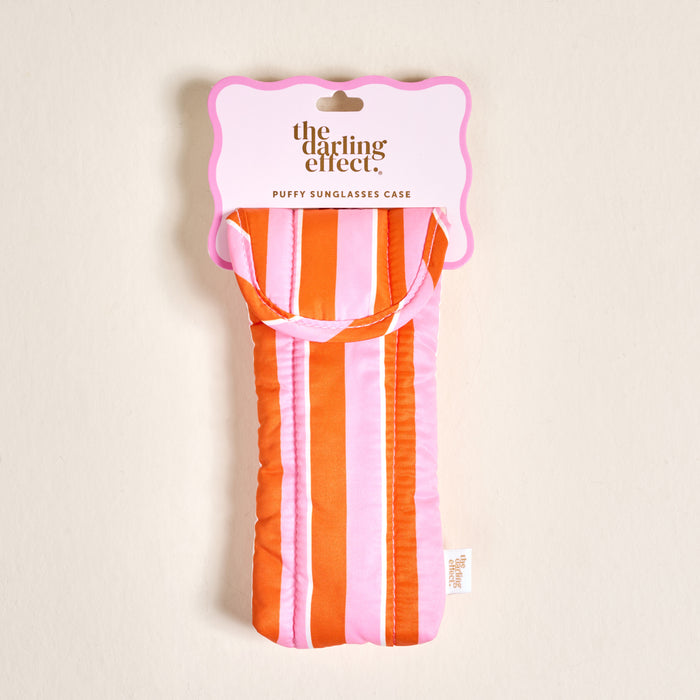 The Darling Effect Sicily Stripes Pink Puffy Sunglasses Case, featuring vertical pink, white, and orange stripes and a secure magnetic flap closure, is shown in its packaging against a plain light background.