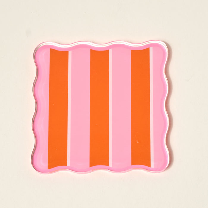 The Darling Effect’s Sicily Stripes Pink Table Talk Acrylic Coaster Set comes in a square tray with wavy edges and vertical pink-orange stripes—ideal for displaying coasters or adding flair to your table décor.