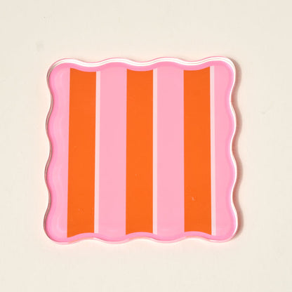 The Darling Effect’s Sicily Stripes Pink Table Talk Acrylic Coaster Set comes in a square tray with wavy edges and vertical pink-orange stripes—ideal for displaying coasters or adding flair to your table décor.