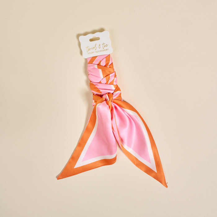 The Darling Effect's Sicily Stripes Pink Twirl & Tie Scarf Accessory features pink and orange stripes, a white tag with "twirl & tie," and offers versatile styling options for any outfit.