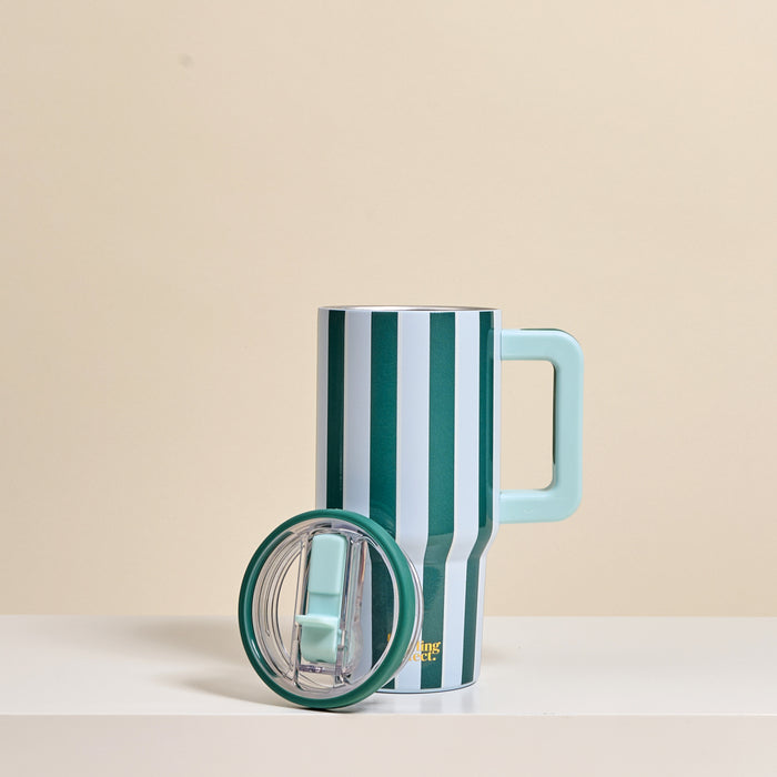 The Darling Effect Sicily Stripes Teal 20 oz Lifestyle Flip Straw Tumbler features vertical green and white stripes, a large light blue handle, and a matching lid, displayed on a light surface with a beige background.