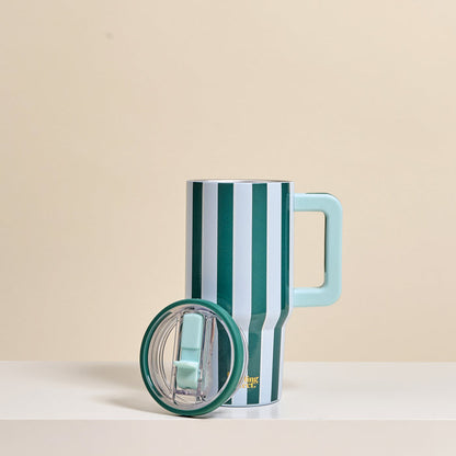 The Darling Effect Sicily Stripes Teal 20 oz Lifestyle Flip Straw Tumbler features vertical green and white stripes, a large light blue handle, and a matching lid, displayed on a light surface with a beige background.